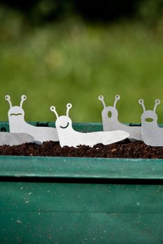 three metal snails sitting on top of dirt in a green container