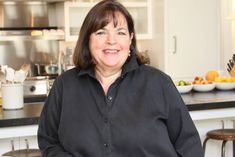 a woman standing in a kitchen next to a counter top with bowls of fruit on it