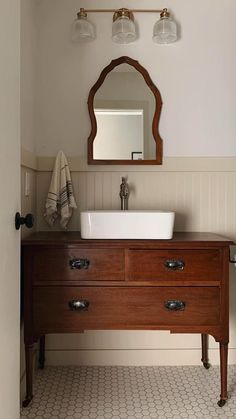 a bathroom sink sitting under a mirror next to a wooden cabinet with two lights on it