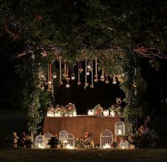 a table with candles and birdcages on it under a tree in the dark