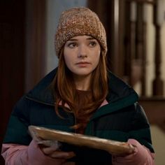 a woman wearing a hat and jacket holding a plate in her hands while looking at the camera