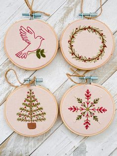 three cross stitch christmas ornaments hanging on a white wooden background with twine and ribbon