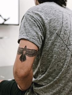 a man with a black bird tattoo on his arm sitting in front of a white wall