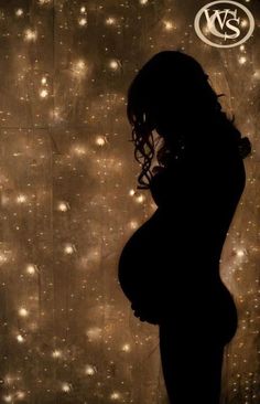 a pregnant woman standing in front of a wall with lights on it's side