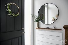 a black door with a round mirror on the wall above it and a white dresser in front of it