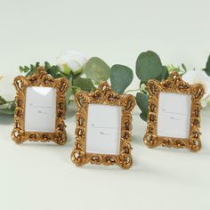 two gold frames sitting next to each other on top of a white table with flowers in the background