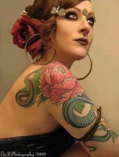 a woman with tattoos and piercings on her arm is posing for the camera while wearing a flower in her hair