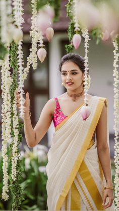 a woman in a yellow and white sari with flowers hanging from the ceiling behind her