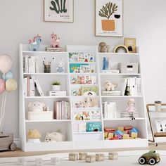 a white book shelf filled with lots of books next to a toy car and balloons