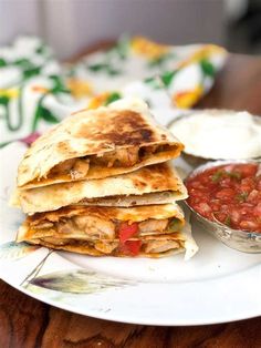 some quesadillas on a plate with salsa and sour cream in the background