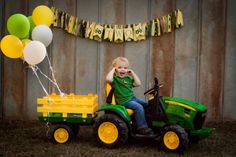 a young boy riding on the back of a green tractor next to a bunch of balloons