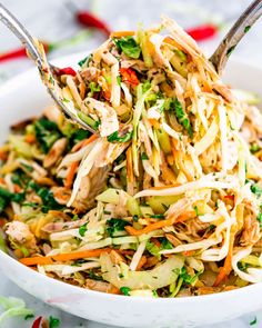 a white bowl filled with coleslaw salad and two serving spoons in it