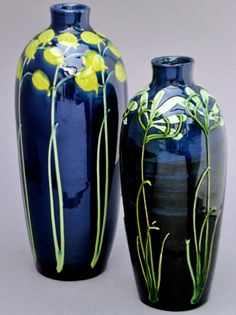 two blue vases sitting side by side on a gray surface with yellow flowers painted on them