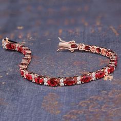 a bracelet with red stones and white diamonds on a blue cloth covered surface, next to a small piece of jewelry