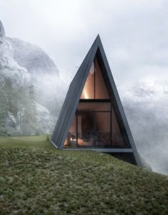 a triangular shaped house sits in the middle of a grassy area with trees and mountains behind it