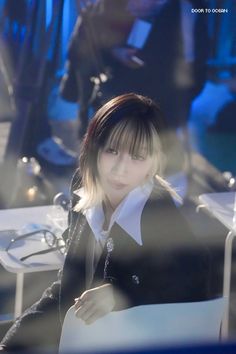 a young woman sitting at a table in front of a laptop computer while wearing a black jacket and white shirt