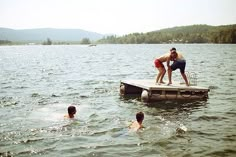 three people are swimming in the water near a dock with a man standing on it