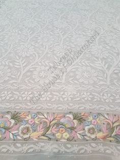 an embroidered table cloth with flowers and leaves on white fabric, in the middle of a room