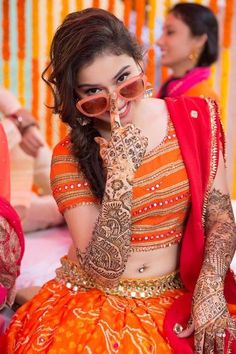 a woman in an orange and red outfit holding her hands up to her face while sitting down