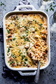 a casserole dish with meat, cheese and noodles in it next to two wine glasses