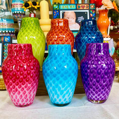 five colorful vases are lined up on a table in front of pictures and other decorative items