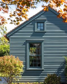 a blue house with an open window on the front and side of it, surrounded by trees