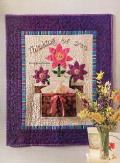 a vase filled with flowers on top of a table next to a purple wall hanging