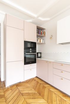 an empty kitchen with pink cabinets and white cupboards on the wall, along with wooden flooring