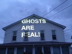 a house with the words ghosts are real projected on it's side in front of an overcast sky