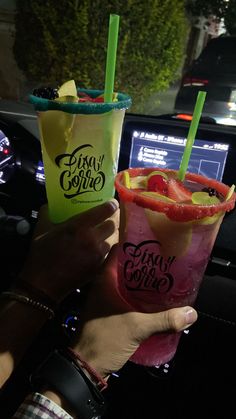 two people are holding up drinks in their hand while driving down the street at night