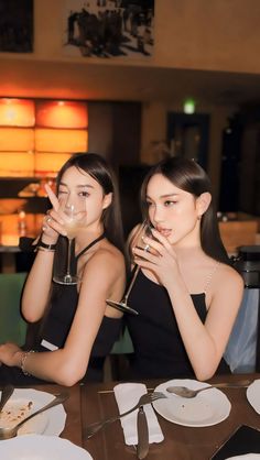 two young women sitting at a table with wine glasses in front of their faces and plates on the table