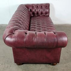 a red leather couch sitting on top of a cement floor