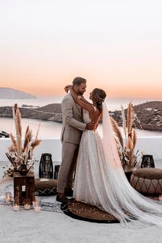 a bride and groom standing next to each other in front of the ocean at sunset