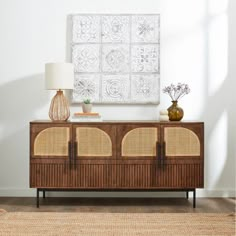 a wooden cabinet with wicker doors and two lamps on top of it in front of a white wall