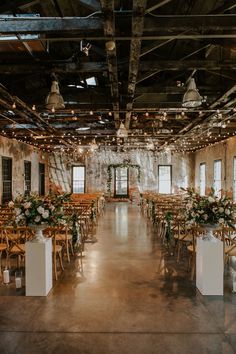 an indoor wedding venue with wooden chairs and floral centerpieces on each side of the aisle