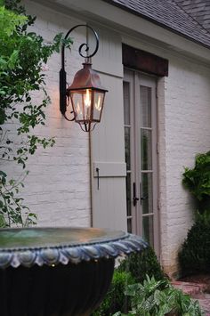 an old fashioned light hanging from the side of a white brick building next to a water fountain