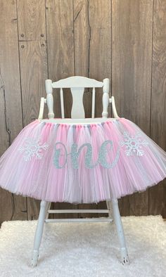 a white chair with pink and blue tulle skirt on it's legs, sitting in front of a wooden wall