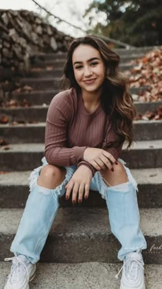 a woman sitting on the steps with her legs crossed and looking at the camera while wearing ripped jeans