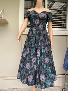 This pre-owned yet New With Tags All That Jazz party dress from the 1980s is a one-of-a-kind find! A call this. Buyers Remorse. It's constructed from a lovely all cotton fabric showing purple and blue muted florals on a black background, making it the perfect choice for a lunch, party, or formal occasion's. It's an original piece and has never been worn before, so it's in pristine condition. This XS size dress has a disco look and is made in the United States. It's perfect for those who love vin Vintage Purple Party Dress, Vintage Floral Print Midi Dress For Party, Retro Floral Print Party Dress, Spring Tea Length Vintage Dress For Party, Spring Tea-length Vintage Dress For Party, Spring Tea-length Vintage Party Dress, Spring Party Vintage Tea-length Dress, Vintage Cocktail Dresses For Party Season, Fitted Tea Length Vintage Dress For Parties