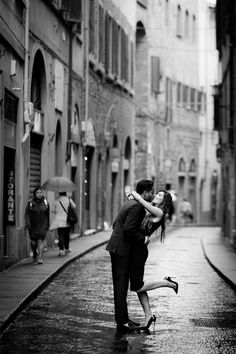 a man and woman kissing in the rain on an alleyway with people walking by