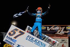 a man standing on top of a race car holding up his arms in the air