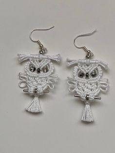 the earrings are made with white yarn and silver metal hooks, which have an owl design on