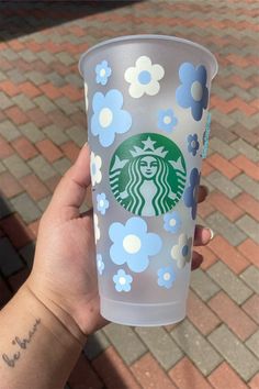 someone holding up a starbucks cup with blue and white flowers painted on it's side