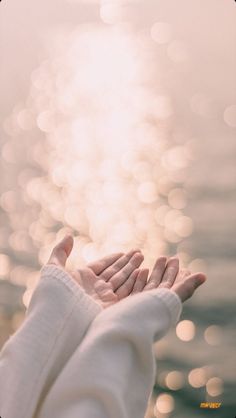 a person holding their hands out to the water with sunlight reflecting on them and blurry in the background