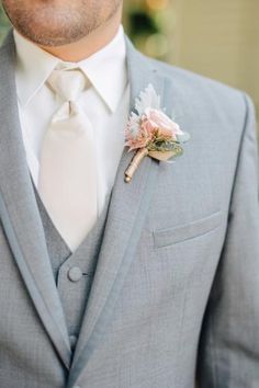 a man in a gray suit and white shirt with a boutonniere on his lapel