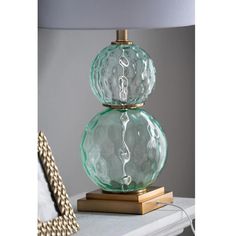 a green glass lamp sitting on top of a white table next to a gold frame