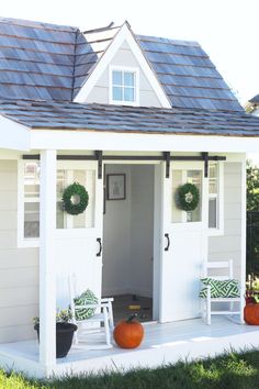 a white shed with two chairs and pumpkins on the porch