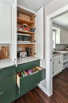 a kitchen with white cabinets and green drawers in the cupboards is open to reveal an assortment of food items