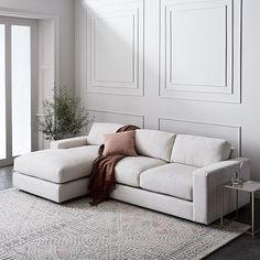 a white couch sitting on top of a rug in a living room next to a window