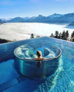 a woman sitting in an outdoor hot tub surrounded by mountains